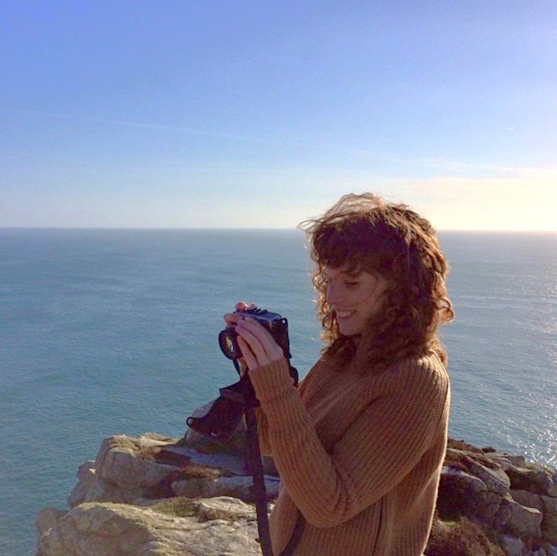 Eloise Rowley standing in front of the sea holding a camera