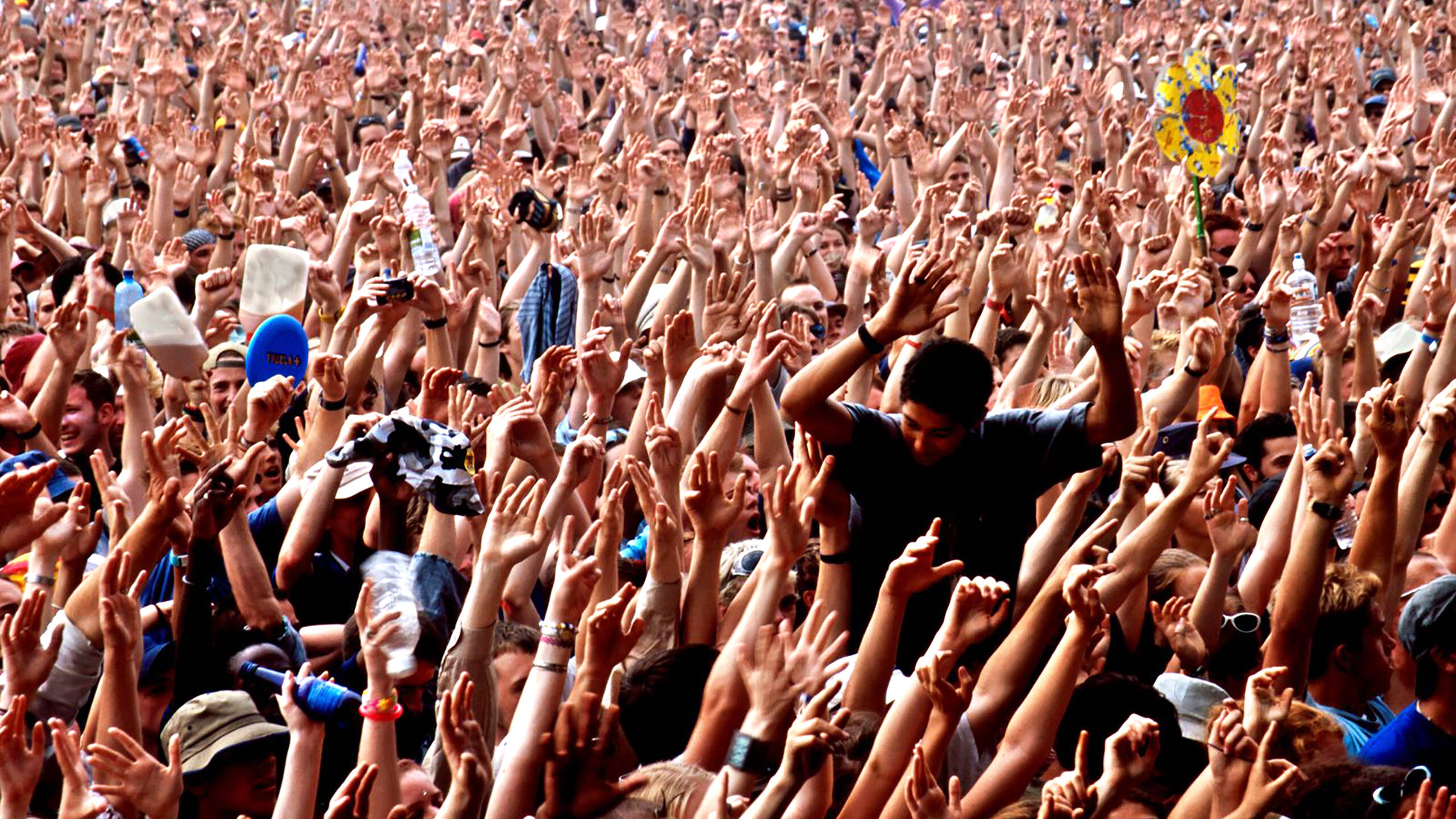 Crowd of people at an outdoor concert, their hands raised