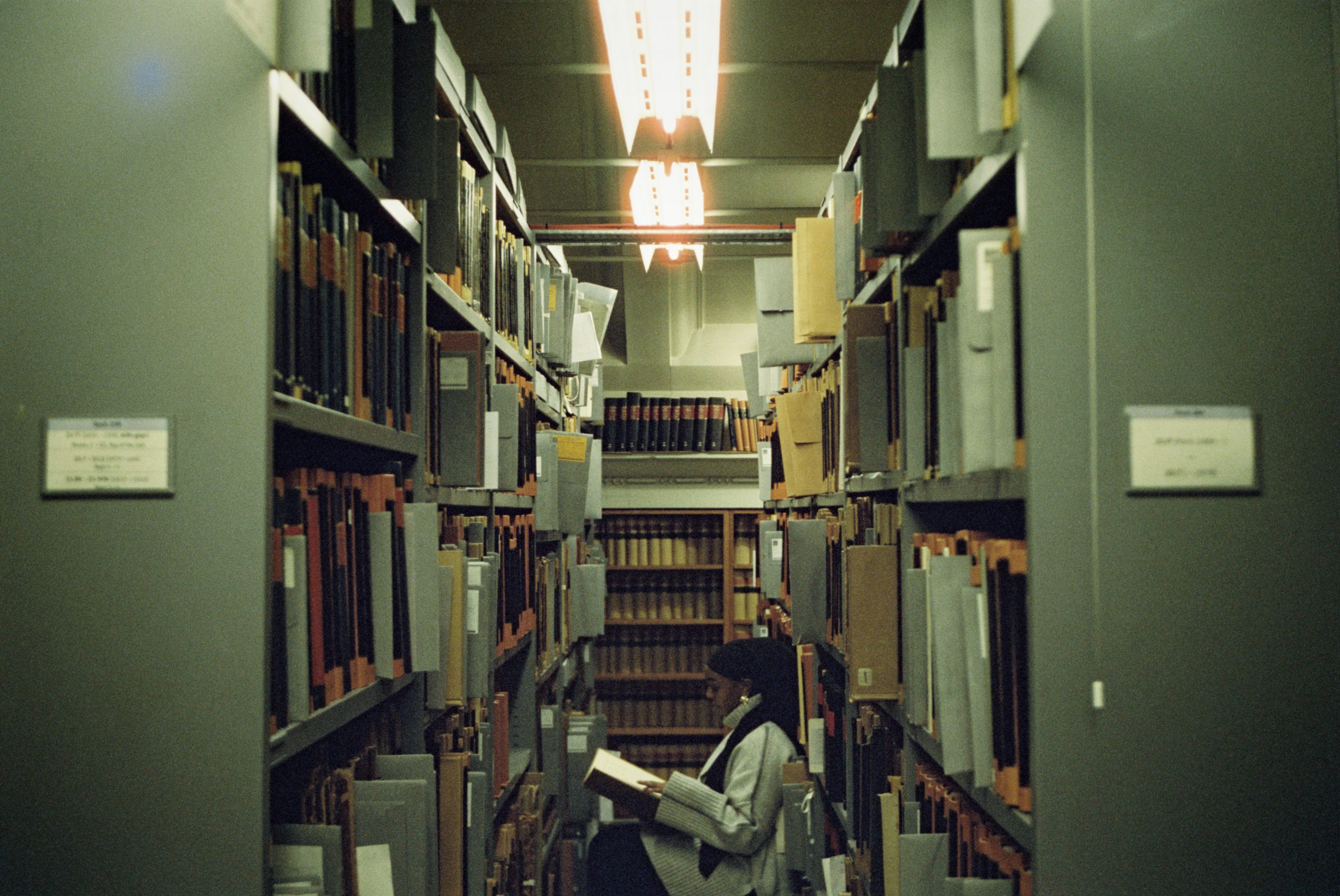 An archive of shelves with folders on, a woman is reading between them